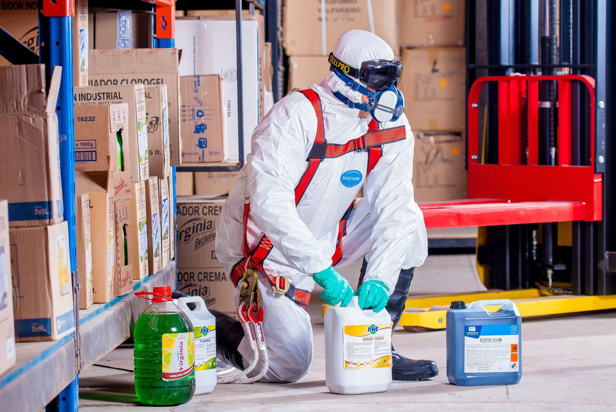Worker in protective clothing handling chemical containers in a warehouse