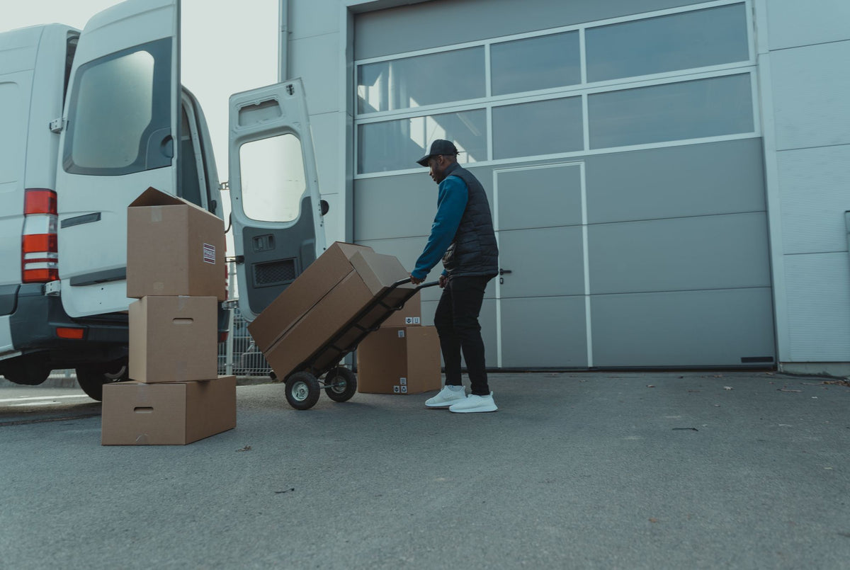 Delivery driver moving cartons on a hand truck beside a van