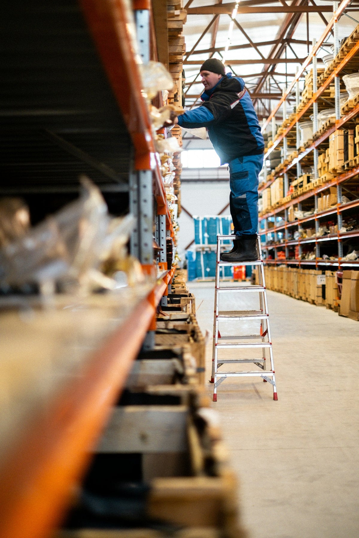 Warehouse worker on an aluminium step ladder picking stock from racking
