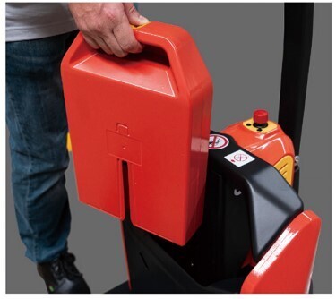 A person holds a red battery pack above a machine, preparing to insert it into the device's compartment.