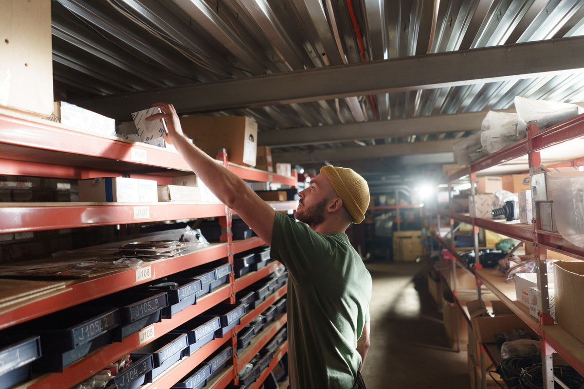 Stockroom worker stretching to reach a top shelf