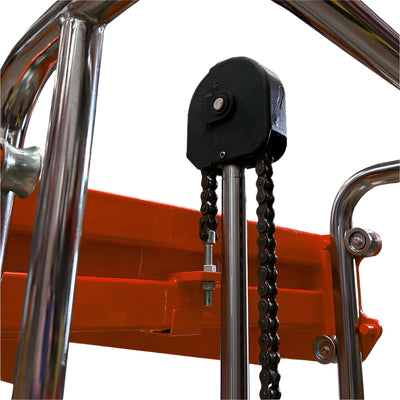 Close-up of a pulley system with a black attachment and metal chain, mounted on a shiny chrome structure against an orange background.