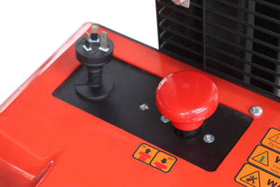 Top view of a red machine control panel featuring an emergency stop button, power socket, and safety warning labels.